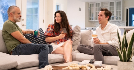 3 people sitting around a coffee table on a couch drinking